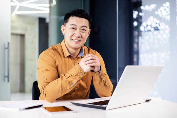 年轻成功的亚洲人在办公室里的肖像，男人微笑着看着相机，在工作中使用笔记本电脑，程序员企业家开发人员穿着衬衫图片下载