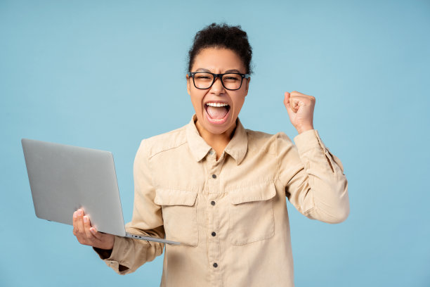 快乐的非裔美国女性戴着眼镜，使用笔记本电脑，庆祝成功，在工作室里摆姿势图片下载