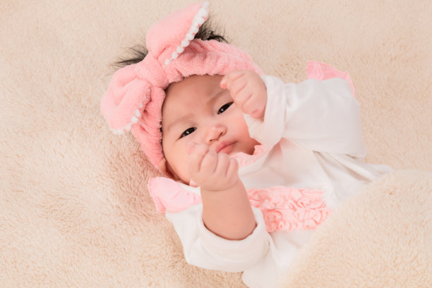 脸部特写，新生儿穿着紧身衣，带着淡粉色的发带，舒适地独自躺在床上，看着家里的镜头，保健和儿科。婴儿用品概念。图片下载