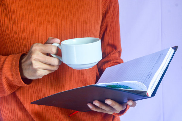 一个穿着橙色t恤的女人的画像，她喝着一杯黑咖啡，读着一本书，做着早晨的活动图片下载