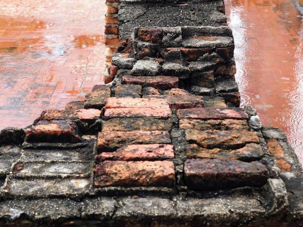 下雨天，一面砖墙撑着一把红伞的照片。图片下载