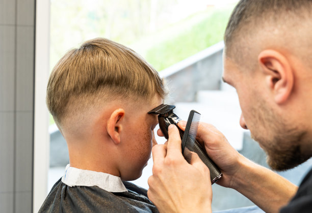 理发店里男人用手梳理小孩头发的特写。男孩用理发师的机器剪头发。男孩在理发店剪头发的照片。图片下载