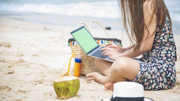 女性旅行者在夏日的海滩蓝天上使用笔记本电脑。特写女子手握休闲装，放松地坐在夏日的热带海滩岛屿上。女士打字笔记本电脑度假商务旅行自由职业图片下载