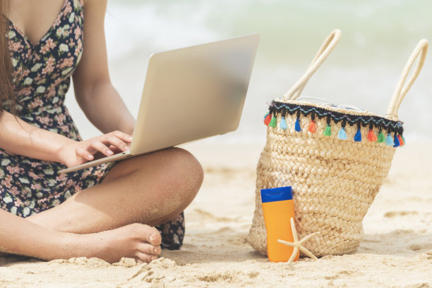 女性旅行者在夏日的海滩蓝天上使用笔记本电脑。特写女子手握休闲装，放松地坐在夏日的热带海滩岛屿上。女士打字笔记本电脑度假商务旅行自由职业图片下载