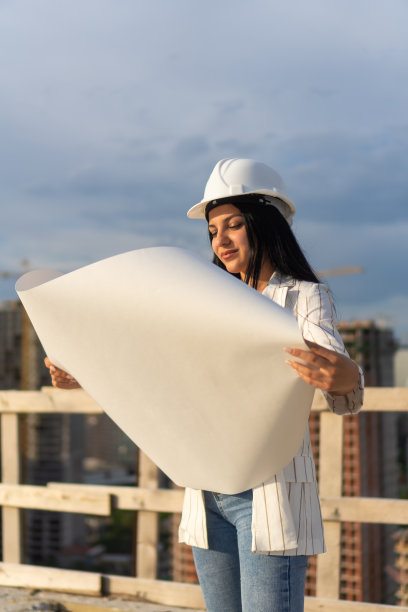 头戴安全帽的年轻建筑师在施工现场查看图纸（竖版照片）图片下载