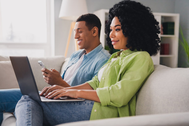 漂亮的年轻男子女孩的照片坐在沙发远程工作上网本设备现代室内室内舒适的日光公寓客厅图片下载