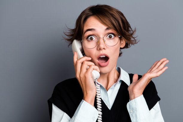 照片中震惊的女人张开嘴，穿着时髦的衣服，说话复古的手机，孤立在灰色的背景下图片下载