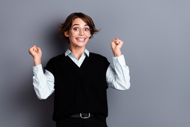 照片中开朗幸运的女ceo戴着黑色马甲眼镜，高举拳头，空旷空间孤立灰色背景图片下载