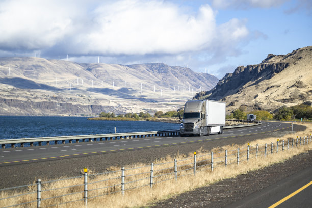 米色大钻机长牵引车半挂车运输货物在干货车半挂车行驶在沿哥伦比亚河分割高速公路与电动风车在山上图片下载
