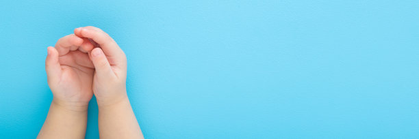 小男孩在浅蓝色的桌子背景上张开手掌。柔和的颜色。特写镜头。视角镜头。空白位置用于文本。宽横幅。自顶向下视图。图片下载