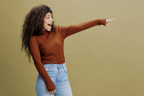 季节性特价优惠。开朗、微笑的卷发拉丁女呆在绿色的墙边，说嘿，看看这个，看看这边，展示在自由的地方复制空间，酷炫的服装销售广告。工作室拍摄孤立图片下载