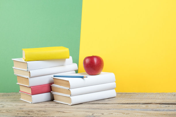 书堆积。书放在木桌和绿色，黄色的背景。回到学校。广告文本的复制空间。图片下载
