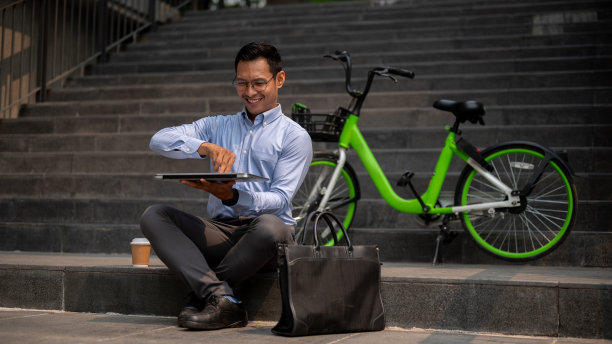 一位亚洲商人坐在户外台阶上，打开笔记本电脑，在户外远程工作。图片下载