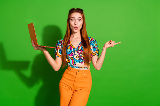 照片中的美女手持上网本点空震惊，穿着时尚复古的衣服孤立在绿色的背景图片下载