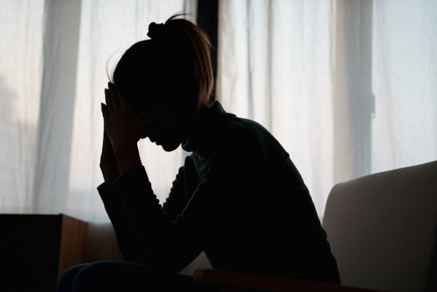 年轻的亚洲女子独自坐在卧室里的剪影照片，感觉不好和不开心，同时思考她的问题，代表失败，失去的爱，抑郁。阴暗、喜怒无常、消极的情绪。图片下载