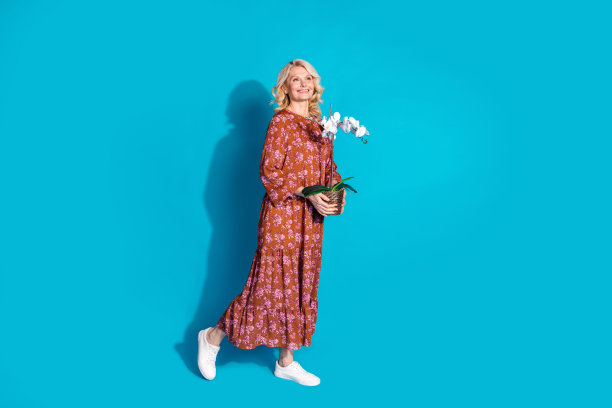 全身照片可爱的可爱的女人穿着棕色的裙子种植鲜花空的空间孤立的蓝色背景图片下载