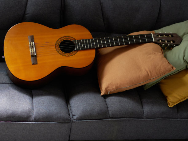 一把灰色的扶手椅上放着一把古典吉他，上面有装饰枕头。图片下载