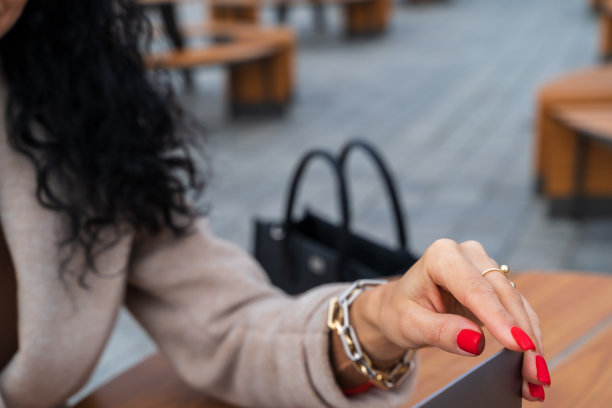 一个涂着鲜红色指甲的女人的手拿着笔记本电脑屏幕，在街上的一家咖啡馆里工作。观念的商业夫人，光明的赤脚夫人图片下载