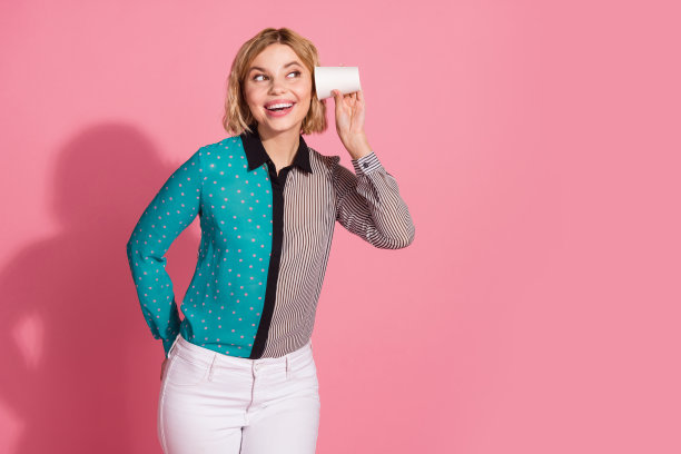 漂亮的年轻女孩的照片肖像听纸杯看空空间穿时髦的条纹青色服装孤立在粉红色的背景图片下载