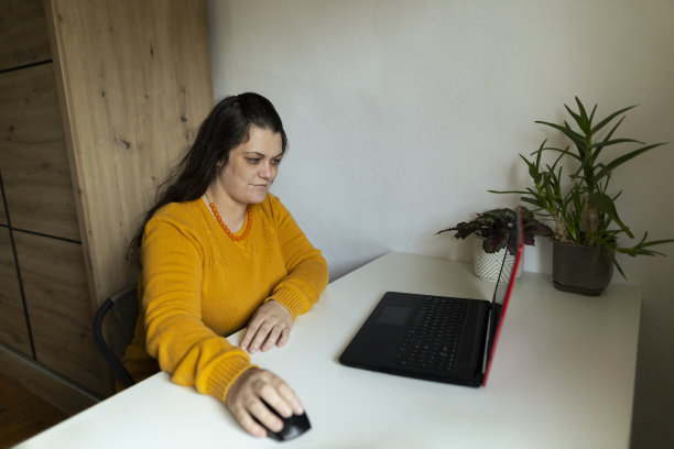 网上购物在家里，美丽的女人使用笔记本电脑在她的家庭工作空间和网上购物。穿着舒适的黄色毛衣。库存图片图片下载