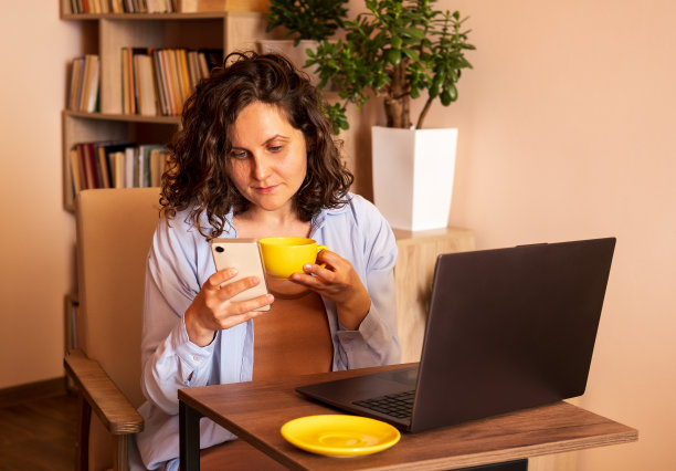 年轻女子在工作场所使用笔记本电脑和手机。图片下载