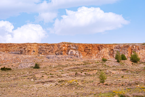 这张照片显示了明亮的蓝天下的岩石悬崖，天空中有零星的云。图片下载