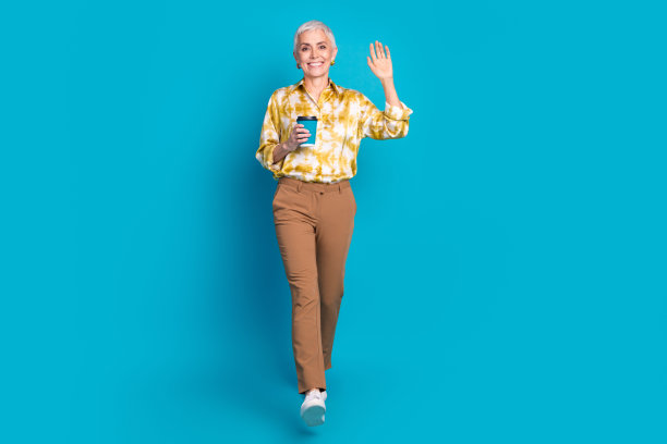 迷人的老年妇女的全身照片走摇臂咖啡纸杯穿着时尚优雅的衣服孤立在蓝色的背景图片下载