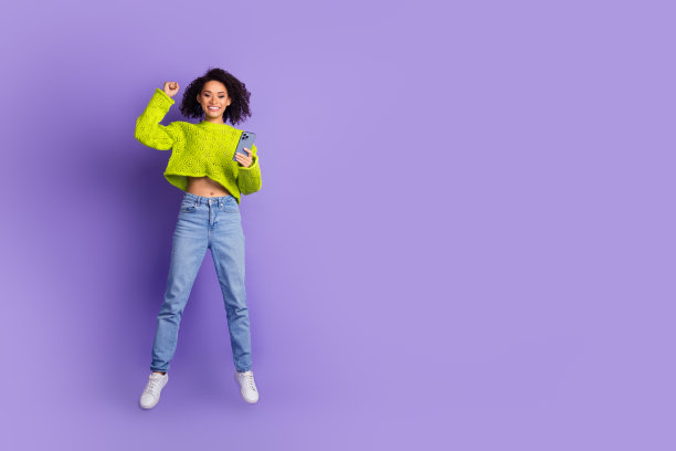 照片卷曲的美国年轻跳跃女孩在毛衣使用手机copyspace网站媒体孤立的紫罗兰色背景图片下载