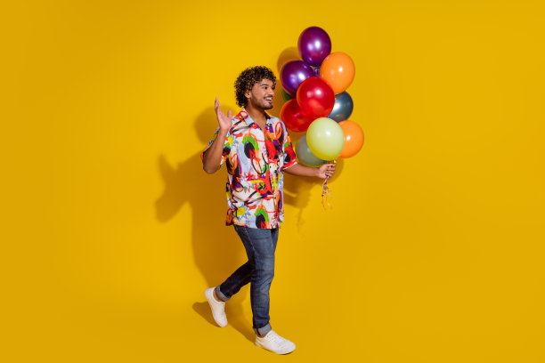 英俊的年轻男性气球走挥手手穿着时尚的彩色服装孤立在黄色背景的全身照片图片下载
