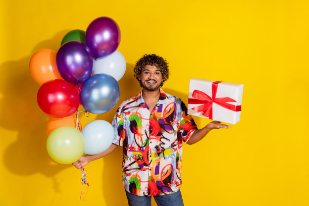 照片中英俊的年轻男子手持气球，穿着时尚的彩色服装，孤立在黄色背景上图片下载