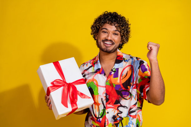 照片肖像英俊的年轻男子拿着礼物赢得庆祝销售穿着时尚的彩色服装孤立的黄色背景图片下载