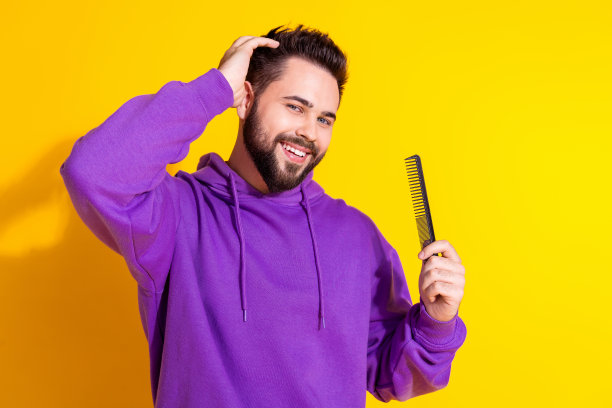 有吸引力的高兴的好男人的照片，穿着时尚的衣服，触摸发型，手持梳子孤立的黄色背景图片下载