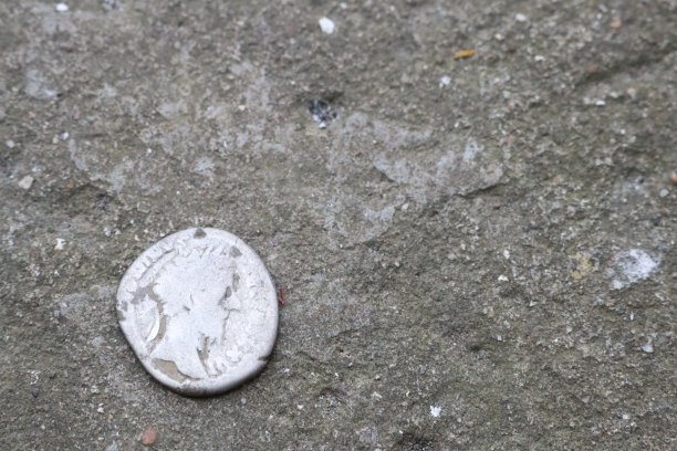 一枚古老的银币被放置在磨损和老化的石头表面，反映了历史和遗产图片下载