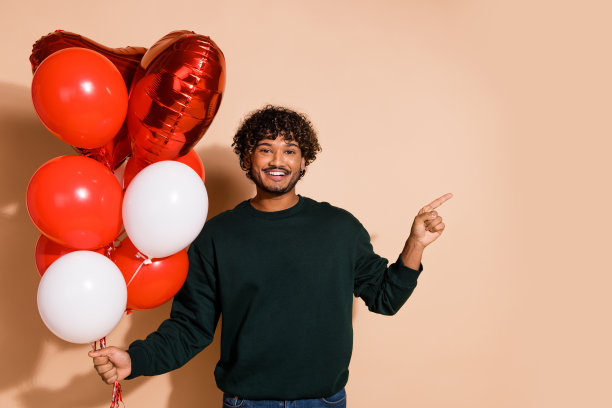 照片中心情好的小伙子穿着运动衫，气球上升，显示空间空旷孤立的米色背景图片下载