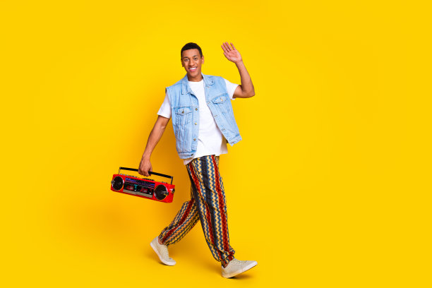 快乐的家伙穿着牛仔裤马甲的全身照片拿着音箱说嗨走空空间孤立的黄色背景图片下载