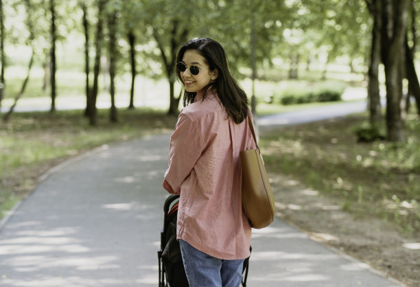 母子在公园里玩耍，推着婴儿车在公园里带着小孩子散步，现代母亲图片下载