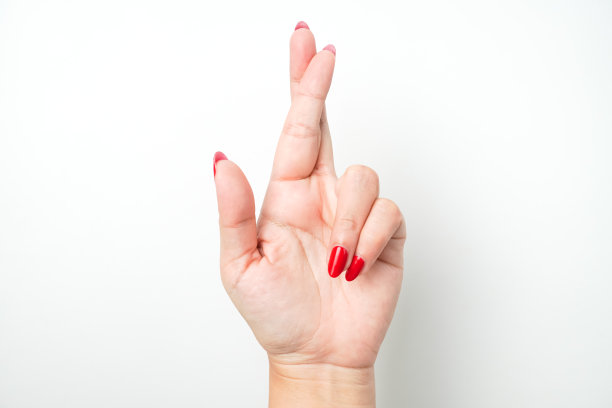 涂着鲜红色指甲油的女性的手形成中指和食指交叉的手势，表示说谎。图片下载