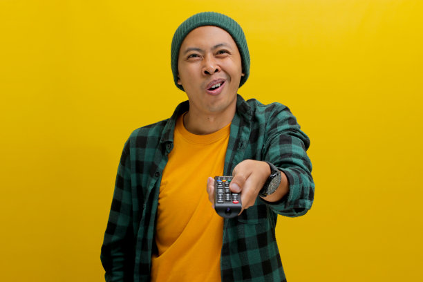 一名亚洲男子拿着电视遥控器，看起来又害怕又惊讶，嘴巴张得大大的，难以置信图片下载