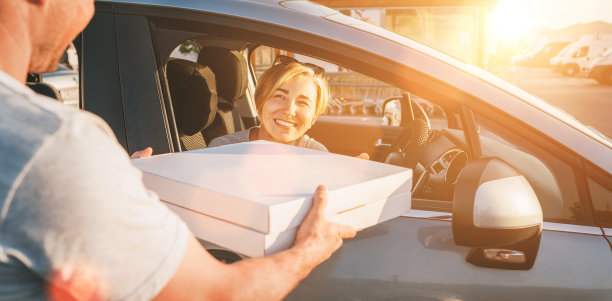 一位年轻的女性坐在汽车的驾驶座上，对着在城市街道上接受两个披萨盒的送货员真诚地微笑。小生意，人际关系，快足餐消费概念照片图片下载