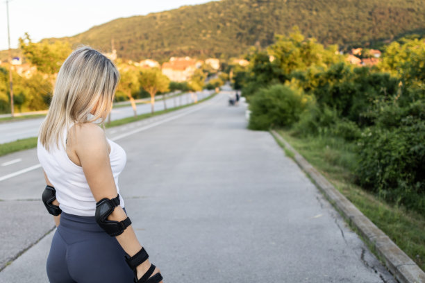 照片上，一个金发美女穿着直排轮滑站在马路上。日落时分穿着运动服的迷人女运动员。图片下载