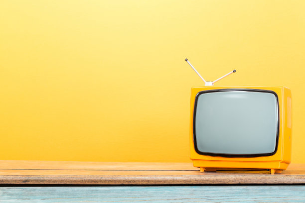 复古的橙色电视接收器在旧木桌前黄墙背景。复古滤镜照片图片下载