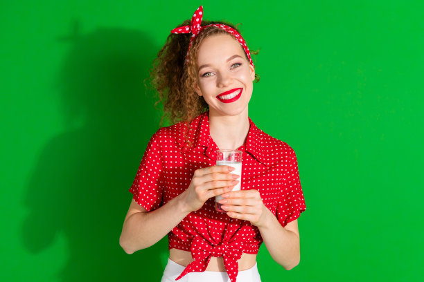 照片肖像可爱的年轻女士拿着牛奶杯穿着时尚的红色复古服装孤立的绿色背景图片下载