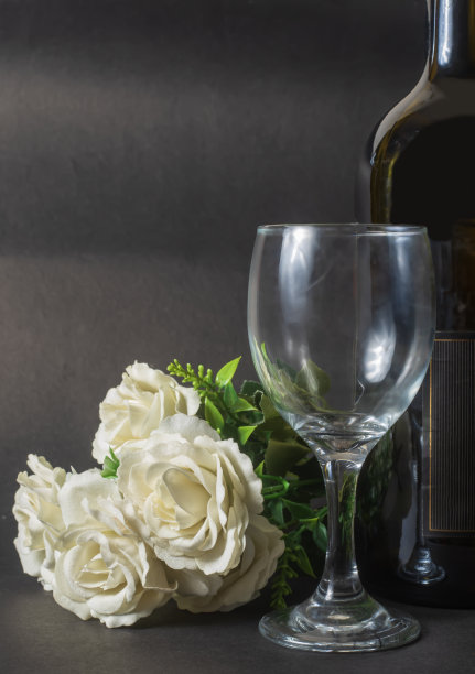 情人节概念:黑色背景上的白玫瑰、酒瓶和空酒杯图片下载