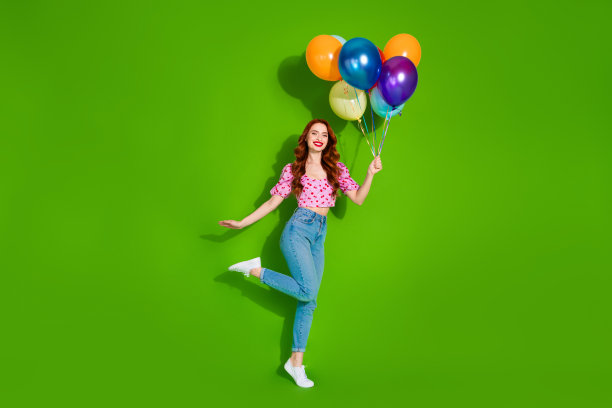 照片的兴奋积极的妇女穿着印花上衣拿着气球束空空间孤立的绿色背景图片下载