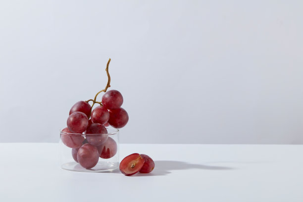 极简风格的照片与紫色的葡萄和实验室工具在白色的背景。一串葡萄装在一个玻璃烧杯里，放在左边，空白的右边用来添加产品或文字图片下载