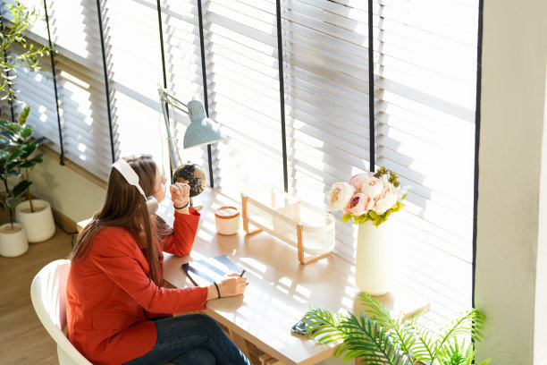 一名身穿红衬衫的年轻女子，在早晨的阳光下，坐在靠窗的客厅里听音乐和工作。在舒适的气氛中快乐图片下载