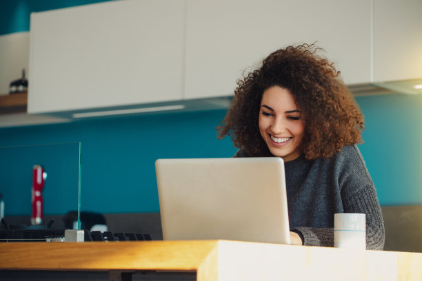 年轻女子在厨房用笔记本电脑在家工作图片下载