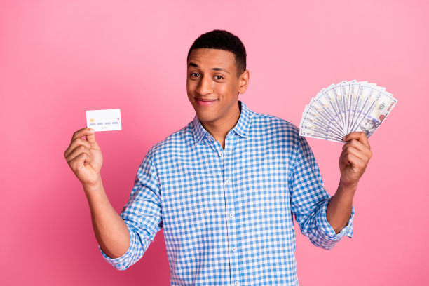 照片时髦的酷家伙穿着格子衬衫持有银行卡美元风扇孤立的粉红色背景图片下载