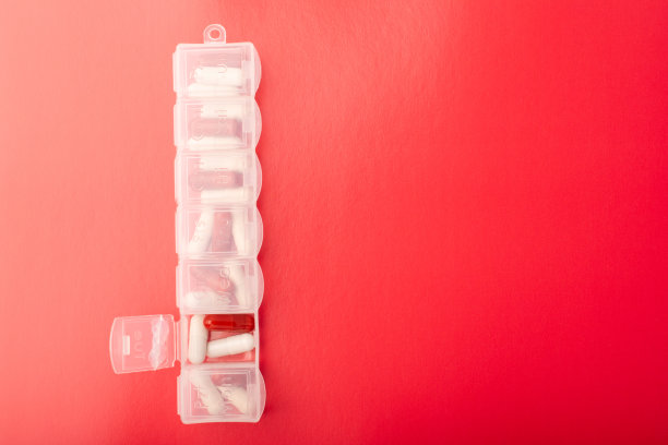 药丸组织者与药丸和补充剂在红色背景，顶视图。胶囊在日常药丸盒。每周药片整理和药片。透明塑料药丸容器和药物。高质量照片图片下载