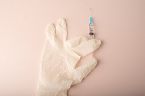 粉红色背景上带有注射器的医用手套。弹性一次性，乳胶无菌贴身防护手套。注入美丽。卫生，医疗保健。美容院。新型冠状病毒肺炎。高质量的照片。图片下载